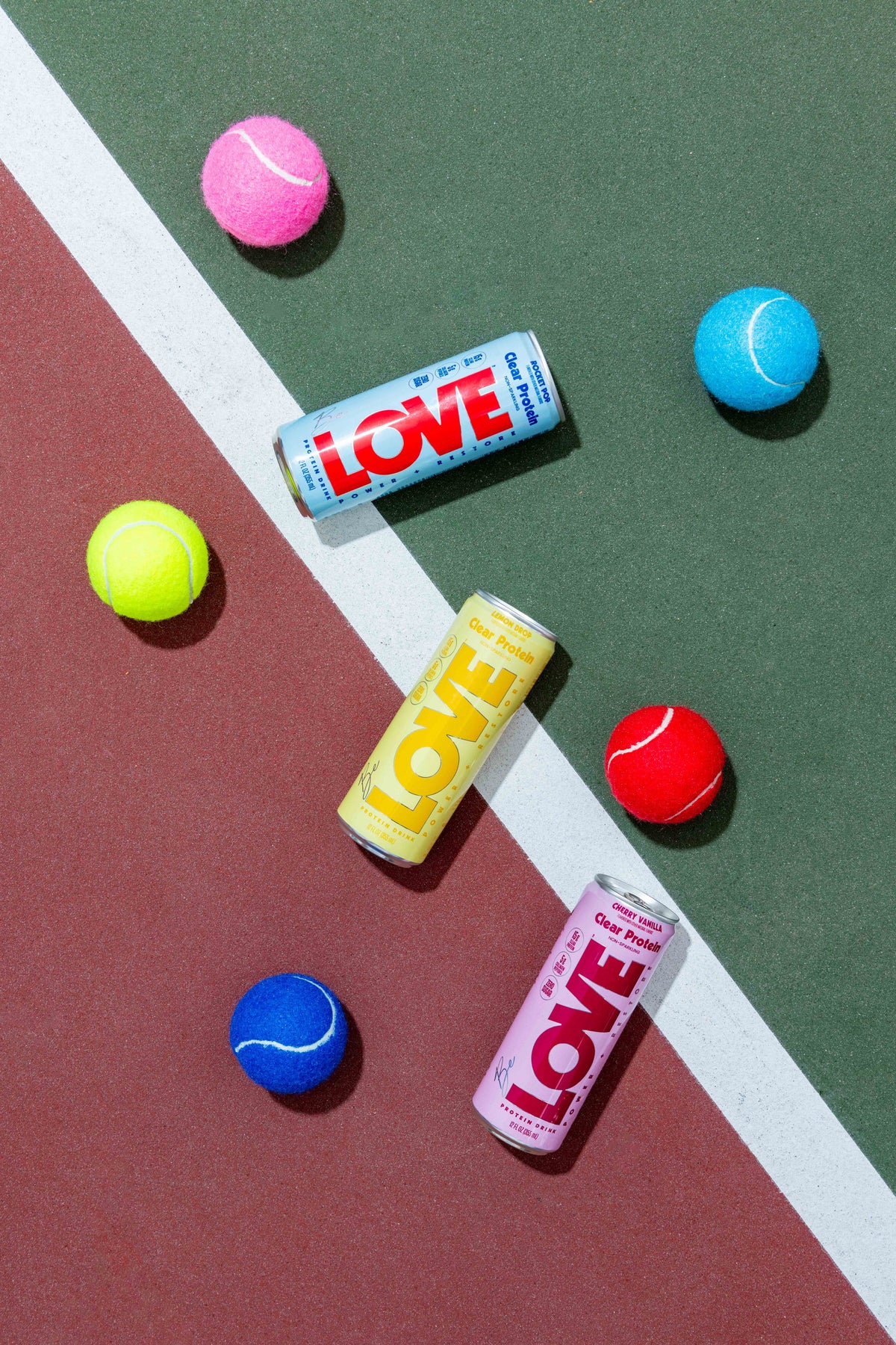 LOVE clear protein cans on a tennis court with colorful tennis balls